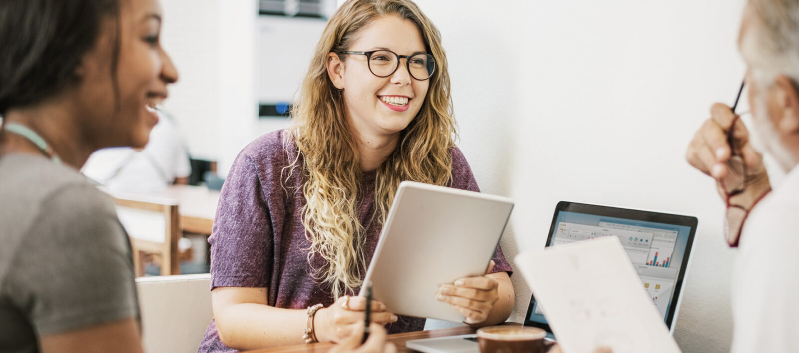 Mehrere Menschen sitzen mit Notizblöcken, Laptop und Kaffee an einem Tisch